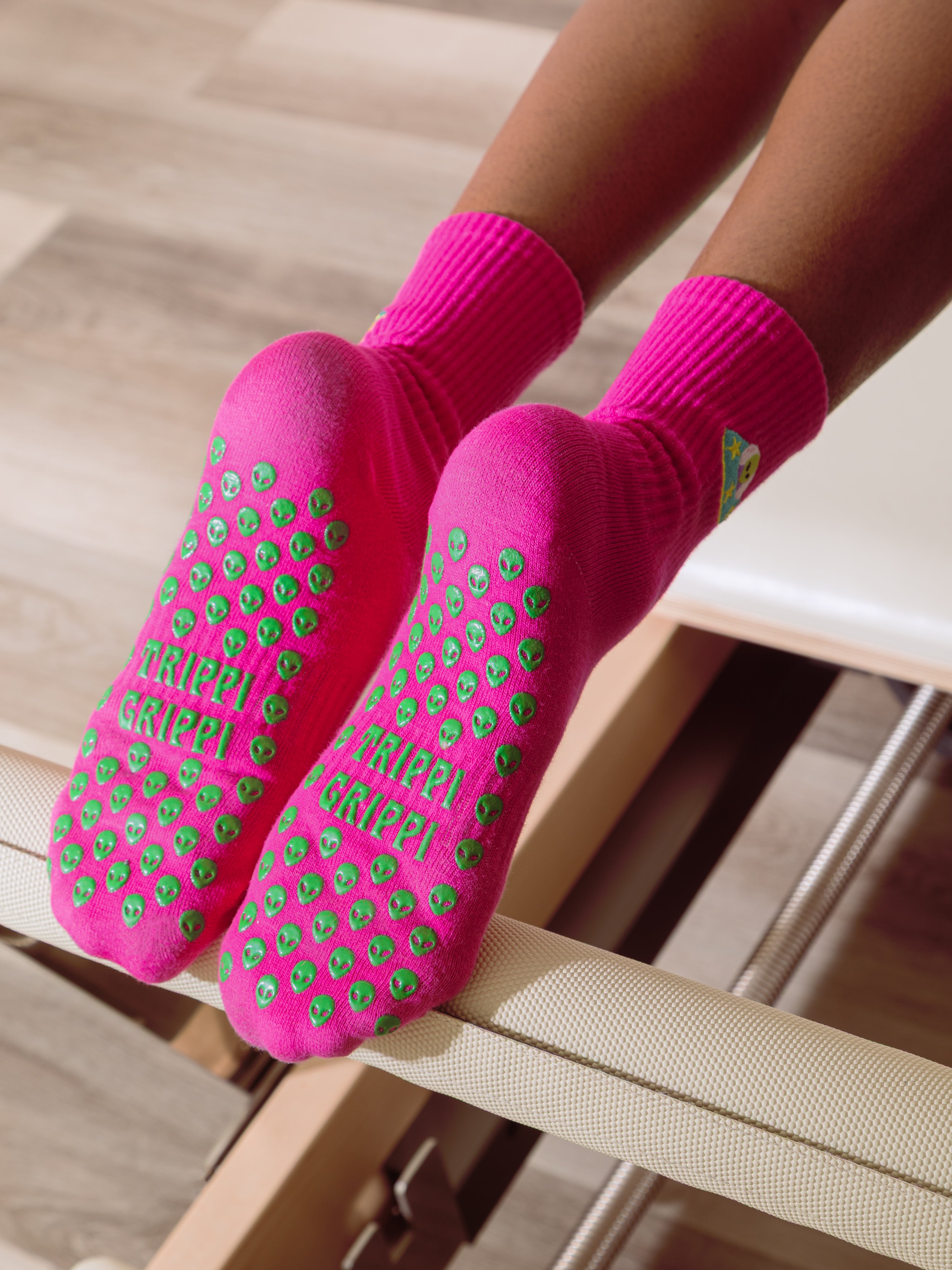 Pink socks with green alien grips on a pilates reformer. Slip-resistant socks for pilates, barre, lagree or yoga.