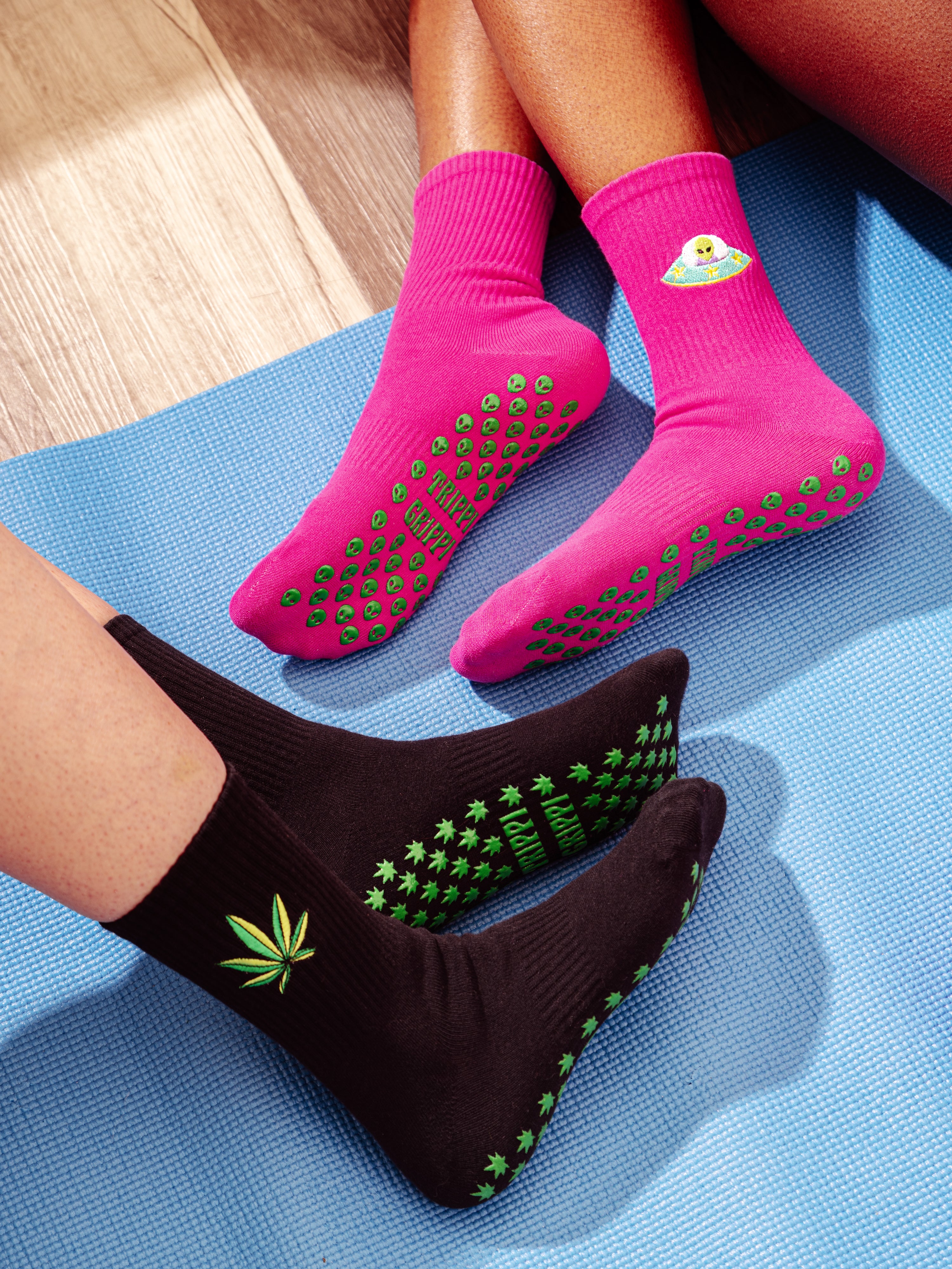Pink and black grip socks with green alien heads and alien heads on a blue mat. Slip-resistant socks for pilates, barre, lagree or yoga.
